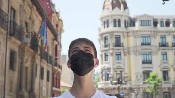 古いヨーロッパの都市の医療用黒いマスクの観光客は、観光スポットを検索するためにスマートフォンの位置情報と電子サービスを使用しています。スペインのオビエド。コロナウイルスのパンデミック後のEUへの旅行 - 映像、動画