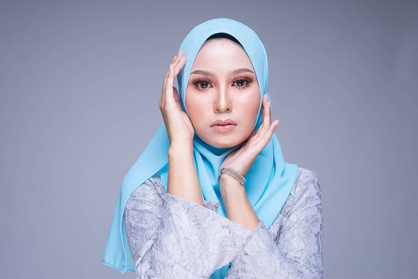 Foto de una hermosa modelo femenina posa usando kebaya y hijab modernos, una ropa de estilo de vida urbano para mujeres musulmanas aisladas sobre un fondo gris. Belleza y hijab concepto de moda
. - Foto, Imagen