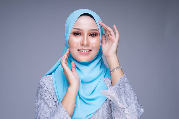 Foto de una hermosa modelo femenina posa usando kebaya y hijab modernos, una ropa de estilo de vida urbano para mujeres musulmanas aisladas sobre un fondo gris. Belleza y hijab concepto de moda
. - Foto, Imagen