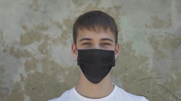 young man laughs and takes off a black medical protective mask against a concrete old wall. Coronavirus Recovery and End of Quarantine and Pandemic - Кадри, відео