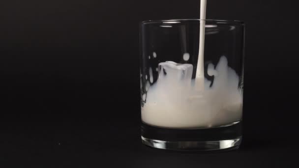 Pouring fresh milk into a glass with ice cubes on a black background. Slow motion splash with drops of fresh white nutritious drink close-up. Slow motion. - Séquence, vidéo
