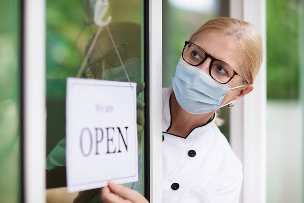 Cafe opening after lockdown. Open sign on front door of restaurant or grocery store. Waiter in apron greeting customer. Welcome message on bakery entrance. Back to work after quarantine. - Foto, Imagem