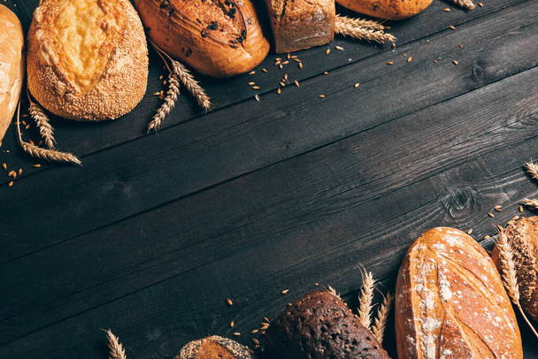 Bread border on wood background with copy space.Different types of bread arranged as frame with spikelets. Bakery, cooking and grocery store concept. - Foto, imagen