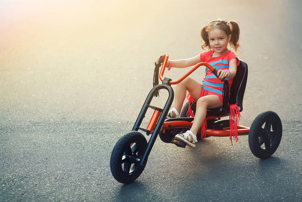 Egy négyéves kislány piros triciklivel jár. Ő lovagol a kifutópályán.  - Fotó, kép