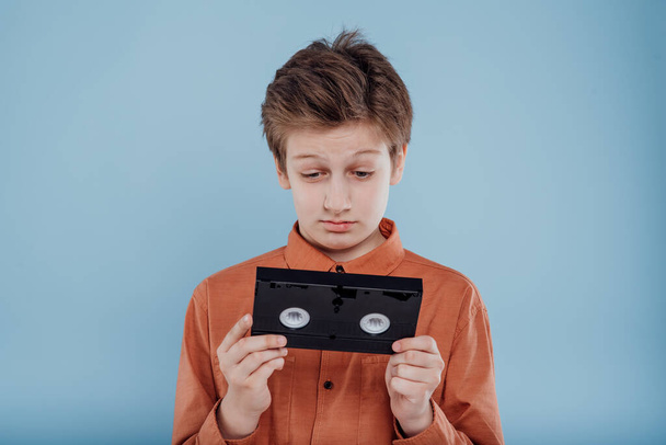 astonished preteen with video tape, isolated on blue background, - Foto, afbeelding