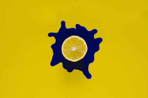 Φέτα λεμόνι σε σκούρο μπλε αφίσα χρώμα που πέφτουν σε κίτρινο φόντο. Ελάχιστη καλοκαιρινή έννοια. - Φωτογραφία, εικόνα