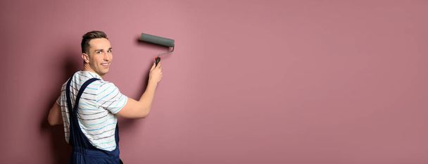Professional decorator with paint roller near pink wall, space for text. Banner design - Foto, imagen