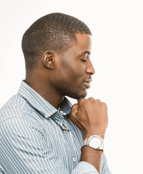 Handsome short-haired businessman touching his chin with fist. Thoughtful African guy wearing striped shirt with expensive wristwatch standing on white background. Profile view portrait. Toned image - Photo, Image