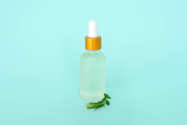 Botella cosmética de vidrio con aceite. Recipiente de vidrio para un producto cosmético para mujeres con pequeñas flores blancas sobre un fondo turquesa
. - Foto, imagen