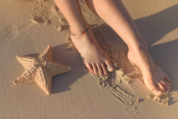 Frauenfüße und Seesterne auf Sand. - Foto, Bild