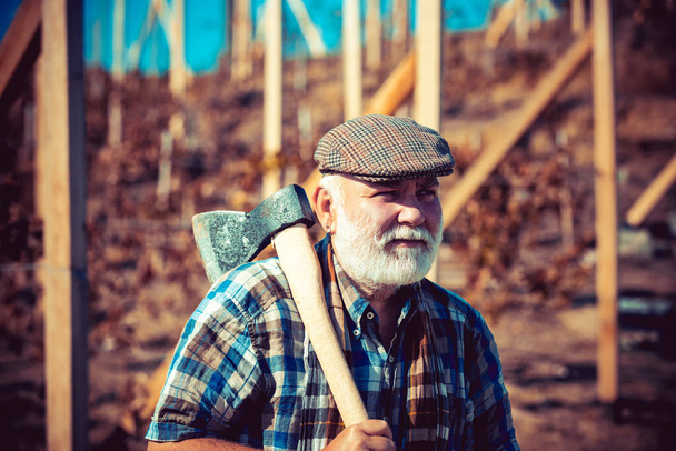 Old bearded man with axe. Portrait of aged smiling man with beard. Vineyard in valley. Happy man with beard and mustache hold axe. Close up portrait. - Φωτογραφία, εικόνα
