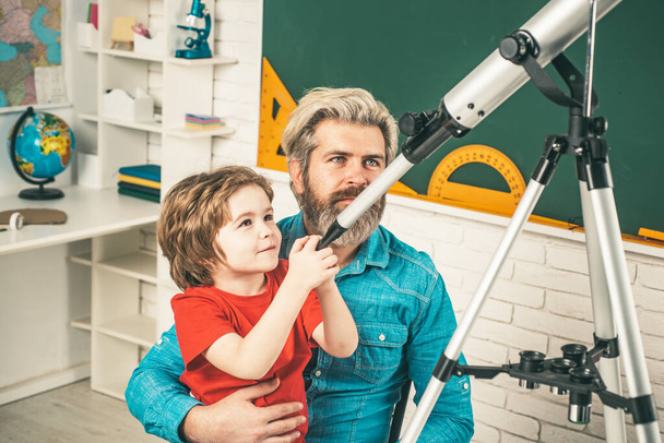 Father teaching son. Cute pupil with funny face hold Astronomy telescope. - Photo, image