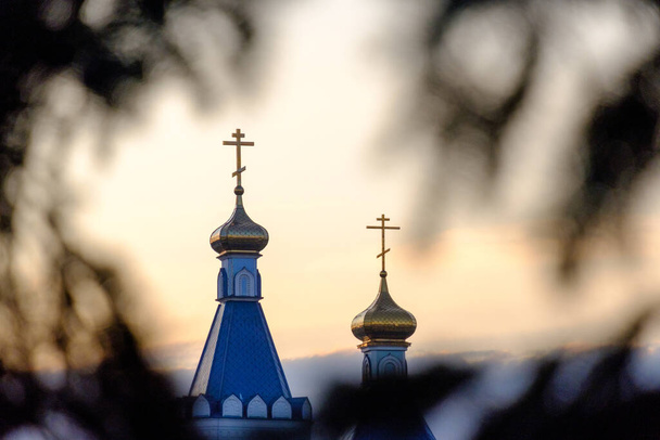 twee torens van de orthodoxe kerk door de takken van bomen bij zonsondergang. harmonie van geloof en natuur - Foto, afbeelding
