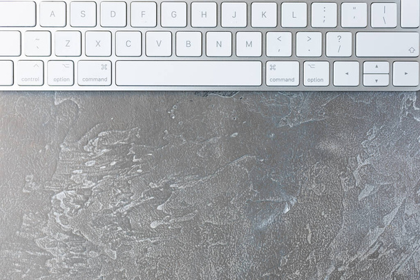 Superficie gris texturizada abstracta con teclado de ordenador blanco. Hermoso fondo rico en color y tonos de hormigón o cemento
. - Foto, Imagen