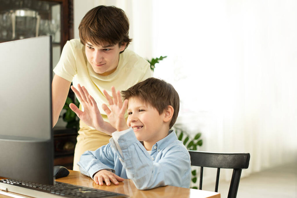Mosolygós fiú és tinédzser csevegnek a neten, és integetnek a számítógép képernyőjének. Karantén és önizoláció a koronavírus miatt. COVID-19 szám - Fotó, kép
