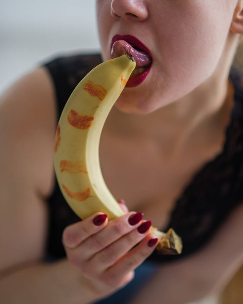 Woman with sensual red lips sucks and licks a banana. Unrecognizable blonde fantasizes about blowjob. Close-up of a female mouth. - Fotografie, Obrázek