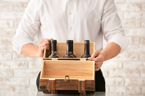 Чоловік з пляшками вина в коробці на цегляному фоні
 - Фото, зображення
