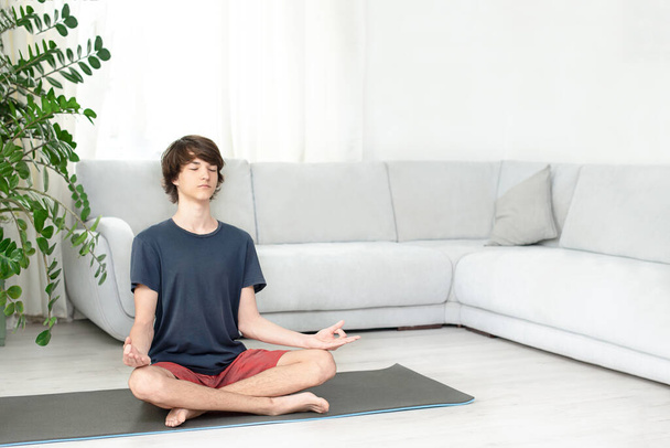 Un jeune homme aux cheveux longs fait du yoga à la maison. Adolescent se trouve en position lotus sur la chambre.Copier l'espace. Place pour le texte - Photo, image