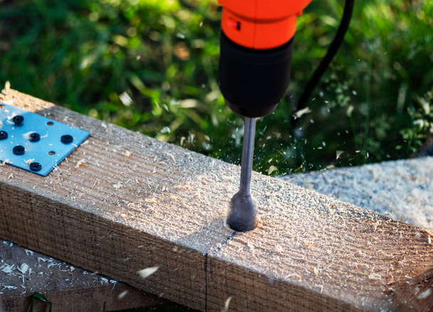 Making holes in a pine beam using an electric drill with wood drilling bit - Foto, afbeelding