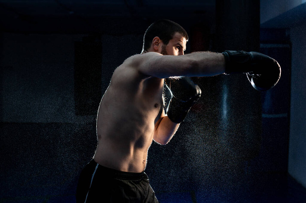 Young male boxer hitting punching bag on black background - Foto, afbeelding