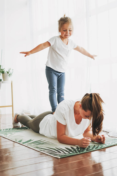 Happy mom and little daughter doing morning exercise together at bright interior home - Фото, изображение