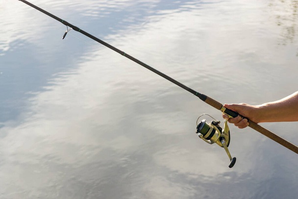 Vishengel in de handen van een visser op het meer. mooie handen met spinnen op de achtergrond van water. concept voor de dag van de visser en de zomer vissen. hobby - Foto, afbeelding