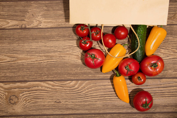 熟したトマトと黄色のコショウをクラフトバッグに入れます。木の板を背景に - 写真・画像