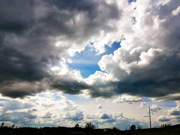 Donkere cumulus wolken hangen boven een smalle strook land. Het licht breekt door de wolken, blauwe lucht. De foto is kort voor zonsondergang genomen. Een buitenwijk van Vitebsk in Belarus. - Foto, afbeelding
