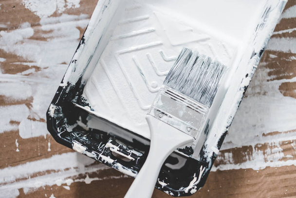 DIY and home improvement concept, close-up of paint tray with white glossy paint and paint brush on it - Valokuva, kuva