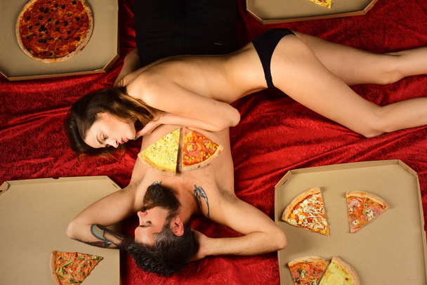 Happy naked loving couple spending time together eating Italian tasty delicious pizza in the bed. Lazy weekend. Couple in love lovers of fast food. Pizza delivery to home. - Foto, Imagen