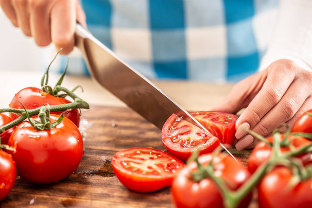 Detal żeńskich rąk krojących pomidora nożem na desce do krojenia z więcej świeżych pomidorów wokół - Zdjęcie, obraz