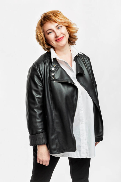 Modern woman with red hair in a white shirt and black leather jacket. Beautiful and happy aging. Isolated on a white background. Vertical. - Foto, immagini