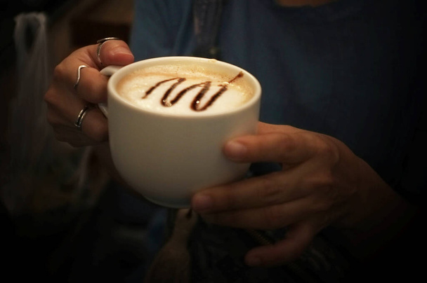 γυναίκα κάθεται και κρατώντας καφέ κύπελλο σε ένα καφέ. - Φωτογραφία, εικόνα