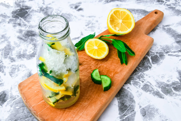 Lemoniada, mojito z posiekaną cytryną i ogórkiem, liście mięty na desce do krojenia, letnie orzeźwiające detox drinki, selektywne skupienie, - Zdjęcie, obraz