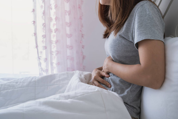 Young woman having stomach ache on the bed. Periods cramp problems concept - Foto, immagini