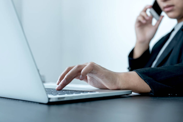 Девушка-бизнесмен разговаривает по телефону с улыбкой, сидя за столом и открывая современный рабочий ноутбук в офисе
. - Фото, изображение