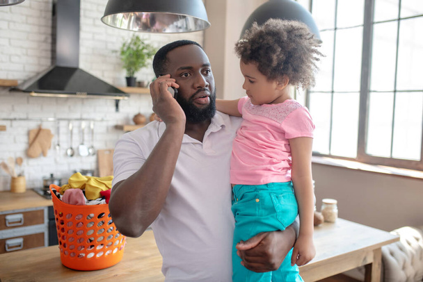 Dark-skinned tall father holding his kid and talking on the phone - Valokuva, kuva