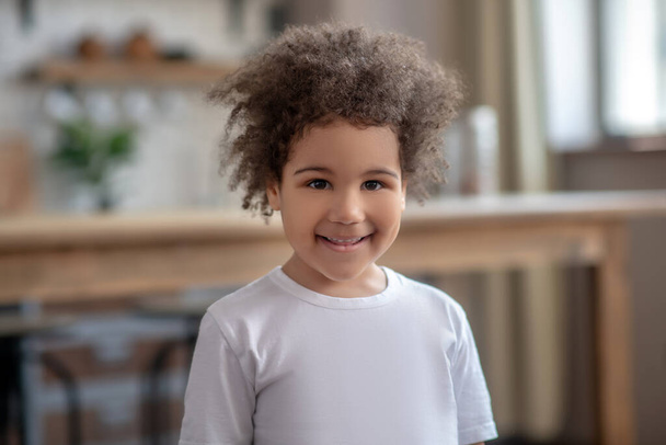 Cute curly-haired kid in a white tshirt smiling nicely - Photo, image