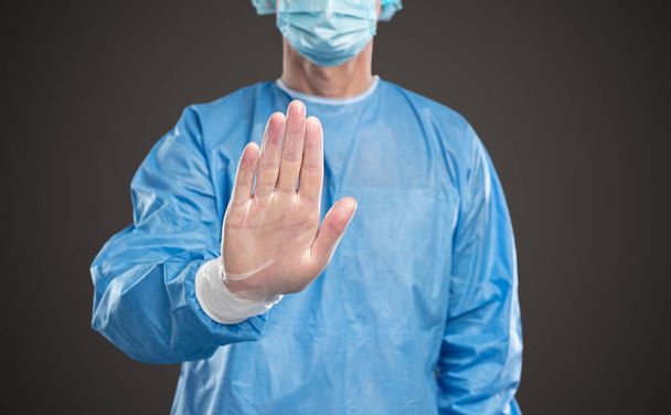 Crop male doctor in protective suit making stop gesture during COVID 19 - 写真・画像