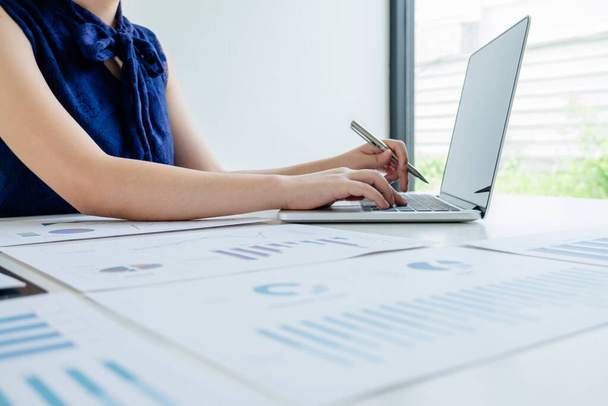 Офисная девушка сидит за столом и использует ноутбук расчета финансового графика, который показывает результаты в офисе
. - Фото, изображение