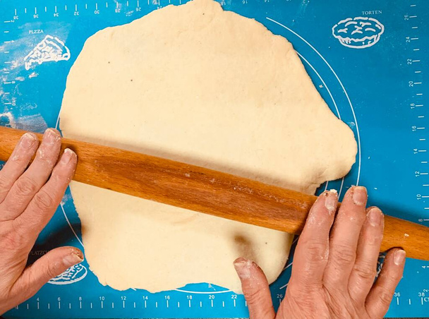 Ręce kobiet ugniatają i zwijają ciasto pszenne z drewnianym pinezką na blasze silikonowej, widok z góry  - Zdjęcie, obraz