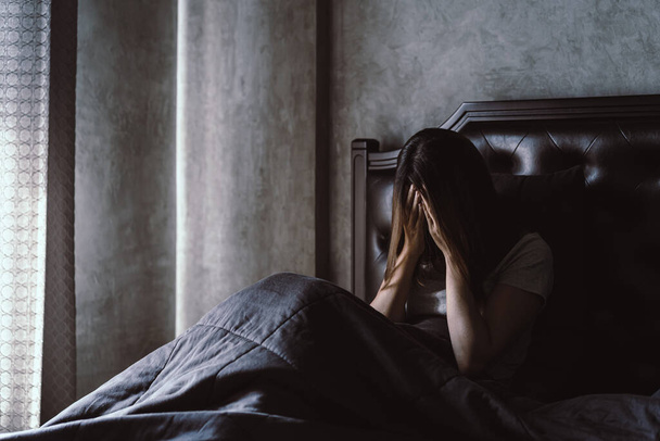 Lonely young woman depressed and stressed sitting in the dark bedroom, Negative emotion concept - 写真・画像