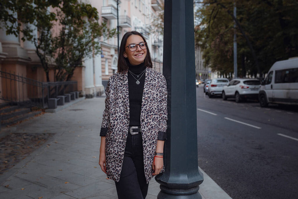 Kaunis nuori brunette nainen kävelee Moskovassa. trendikkäässä leoparditakissa. Hymyilemässä ja kävelemässä kaupungilla. Shoppailu. - Valokuva, kuva