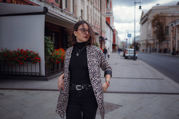 Linda jovem morena caminha em Moscou. Com um casaco de leopardo na moda. Sorrindo e caminhando pela cidade. Ir às compras
. - Foto, Imagem
