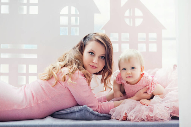 mother plays with her daughter at the window in pink dresses. mother's day. - Foto, Bild