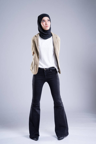 灰色の背景にヒジャーブを持つカジュアルなトップとベルボトムジーンズでイスラム教徒のアジアの女性の高いファッションの肖像画。ヒジャーブファッションのためのファッション編集コンセプト。全長スタジオポートレート. - 写真・画像