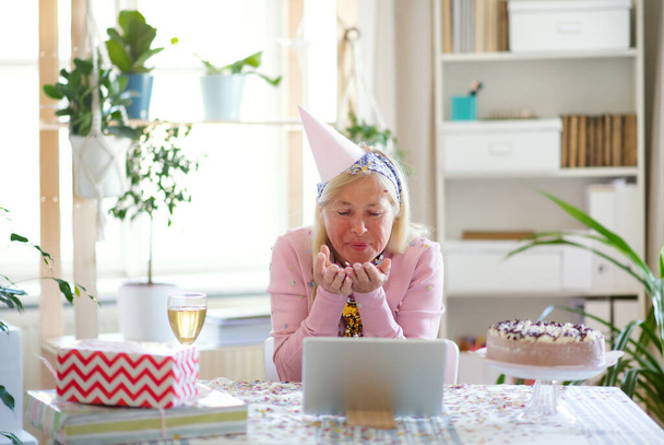 Старшая женщина с ноутбуком дома, празднует день рождения на расстоянии
. - Фото, изображение