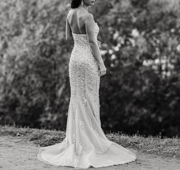 Наречена в елегантній білій сукні з відкритою спиною стоїть з нею до камери. день весілля, весільна сукня з відкритою спиною. Мереживо, мереживна сукня
 - Фото, зображення