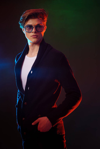 Cool stylish man in black jacket and sunglasses. High Fashion male model posing on black background. - Foto, afbeelding