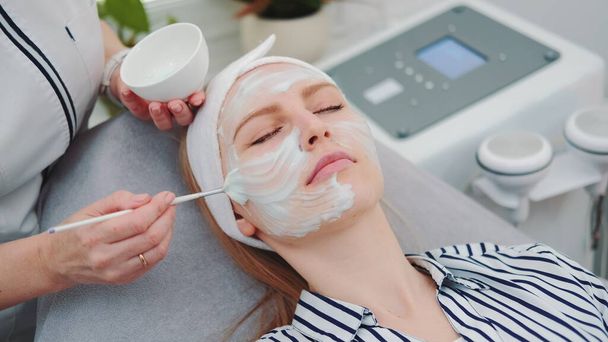 Mediana inyección de esteticista poner máscara de crema en la cara de las mujeres en el salón de belleza
 - Foto, Imagen